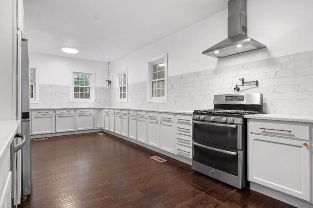 kitchen with stainless steel gas stove, dark wood-type flooring, white cabinets, and wall chimney range hood