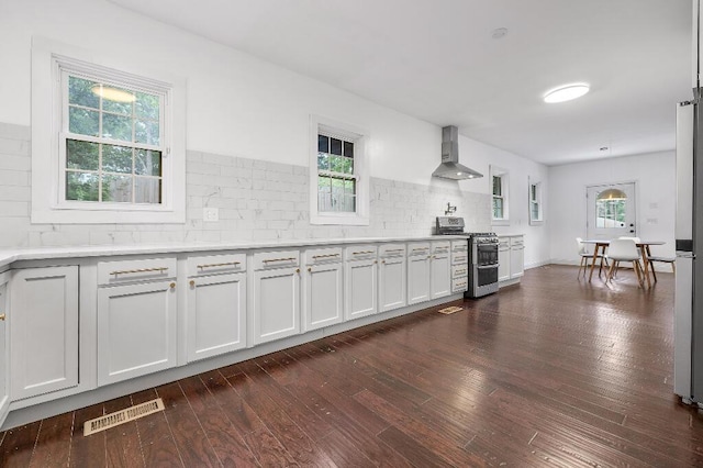 kitchen with dark wood-style floors, double oven range, visible vents, wall chimney exhaust hood, and backsplash