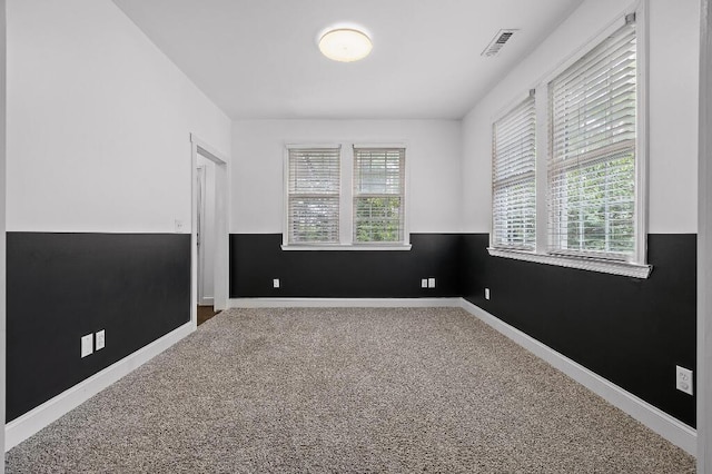 empty room with a wainscoted wall, carpet, visible vents, and a wealth of natural light