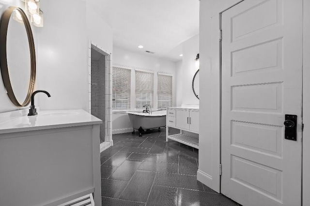 full bathroom featuring visible vents, baseboards, a soaking tub, two vanities, and a sink