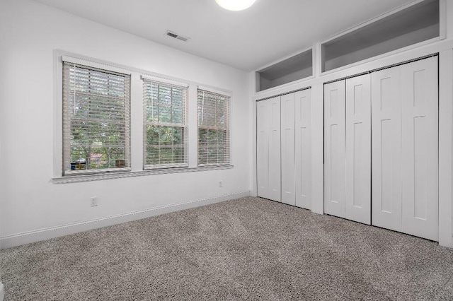 unfurnished bedroom featuring visible vents, carpet flooring, baseboards, and multiple closets