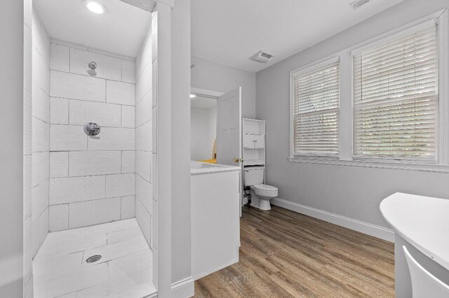 full bath featuring visible vents, baseboards, toilet, tiled shower, and wood finished floors