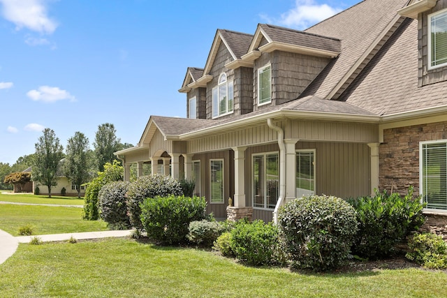 view of home's exterior with stone siding, a lawn, covered porch, and a shingled roof