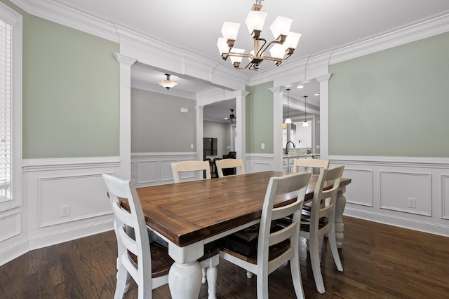 dining space with crown molding, ceiling fan, dark wood finished floors, decorative columns, and wainscoting