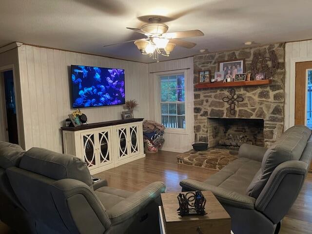 living room with wood walls, ceiling fan, a fireplace, and wood-type flooring