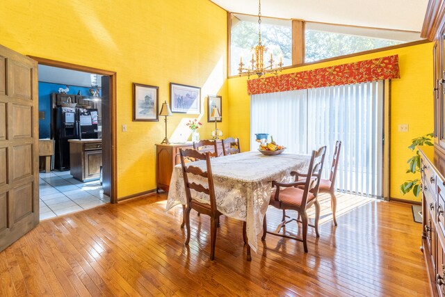 dining room with high vaulted ceiling, an inviting chandelier, and light hardwood / wood-style flooring