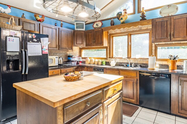 kitchen with light tile patterned floors, black appliances, wooden counters, a center island, and sink