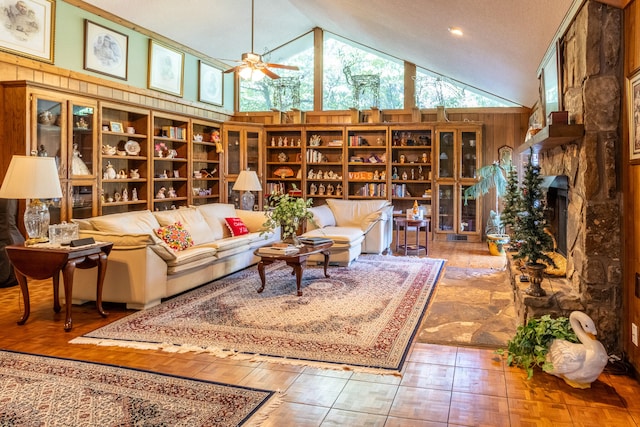 living room featuring wooden walls, hardwood / wood-style floors, ceiling fan, a stone fireplace, and high vaulted ceiling