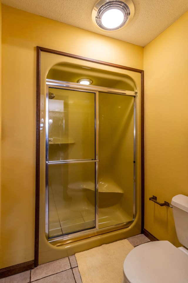 bathroom featuring a textured ceiling, a shower with shower door, toilet, and tile patterned flooring