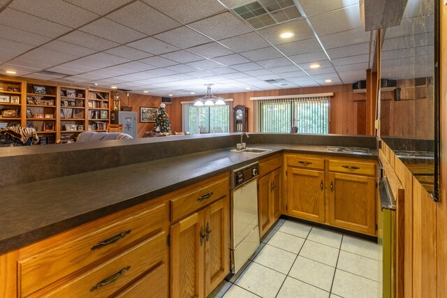 kitchen with hanging light fixtures, light tile patterned floors, white dishwasher, sink, and kitchen peninsula