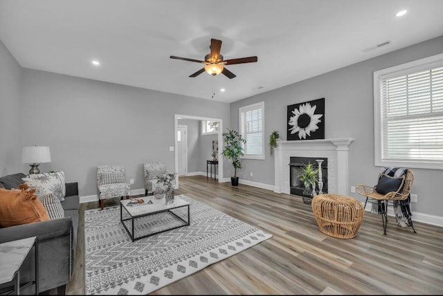 living room featuring a healthy amount of sunlight, ceiling fan, light hardwood / wood-style flooring, and a fireplace