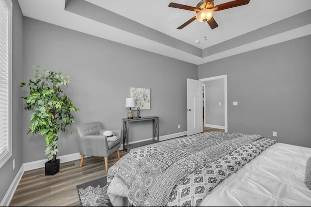 bedroom with hardwood / wood-style floors, ceiling fan, and a raised ceiling