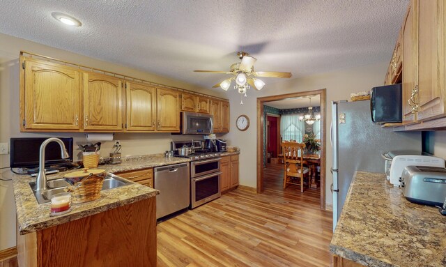 kitchen with ceiling fan with notable chandelier, sink, light hardwood / wood-style flooring, a textured ceiling, and appliances with stainless steel finishes