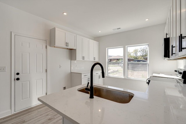 kitchen featuring light stone countertops, stove, sink, light hardwood / wood-style floors, and white cabinetry