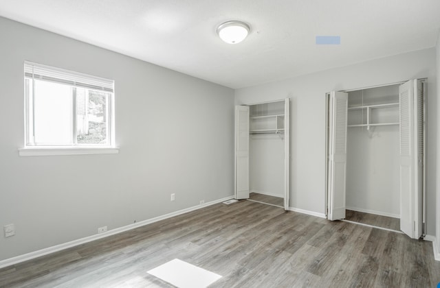 unfurnished bedroom with hardwood / wood-style floors and two closets