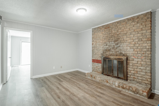 unfurnished living room featuring a textured ceiling, light hardwood / wood-style flooring, a brick fireplace, and crown molding