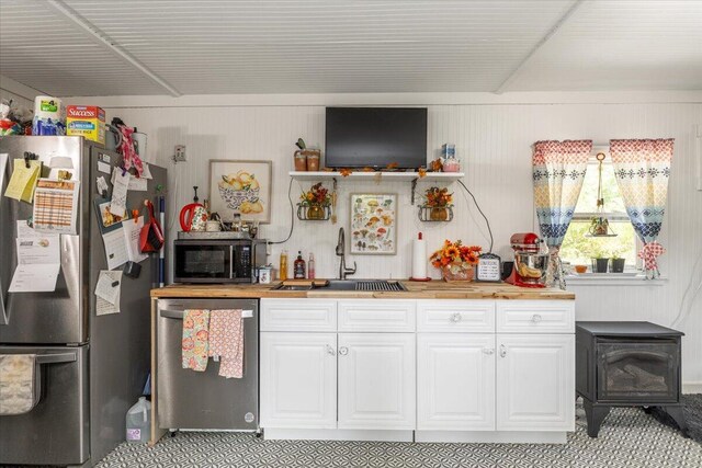 kitchen featuring white cabinetry, butcher block countertops, a wood stove, sink, and appliances with stainless steel finishes