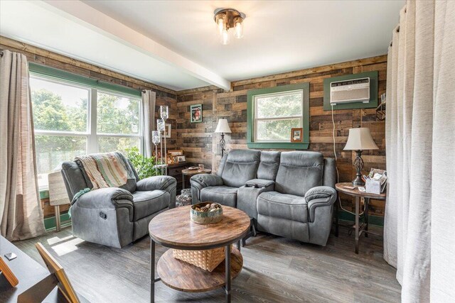 living room with a wall unit AC, hardwood / wood-style flooring, beam ceiling, and a healthy amount of sunlight