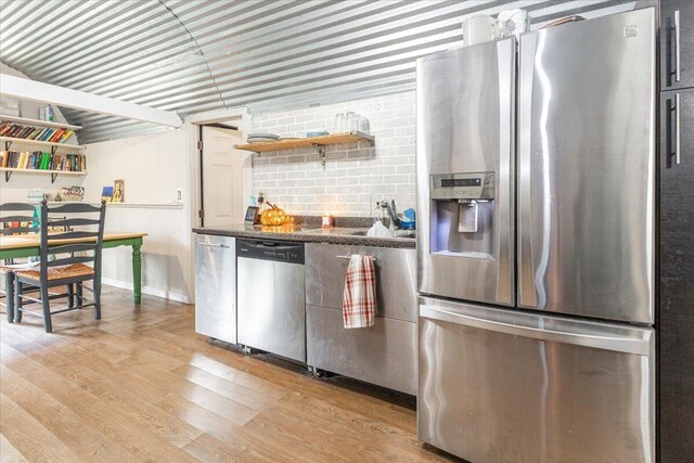 kitchen with light wood-type flooring, appliances with stainless steel finishes, and dark stone counters