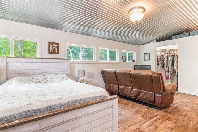 bedroom featuring vaulted ceiling, a spacious closet, a closet, wood-type flooring, and wooden walls