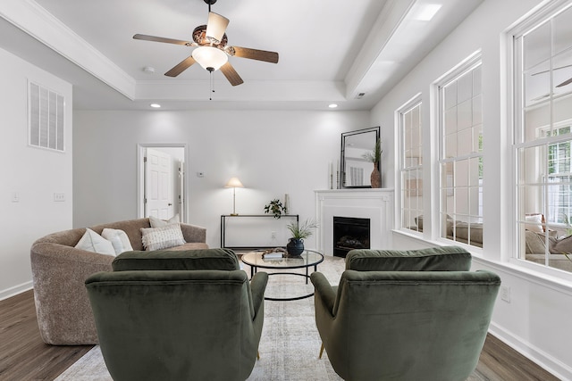 living room with a raised ceiling, ceiling fan, ornamental molding, and dark hardwood / wood-style flooring