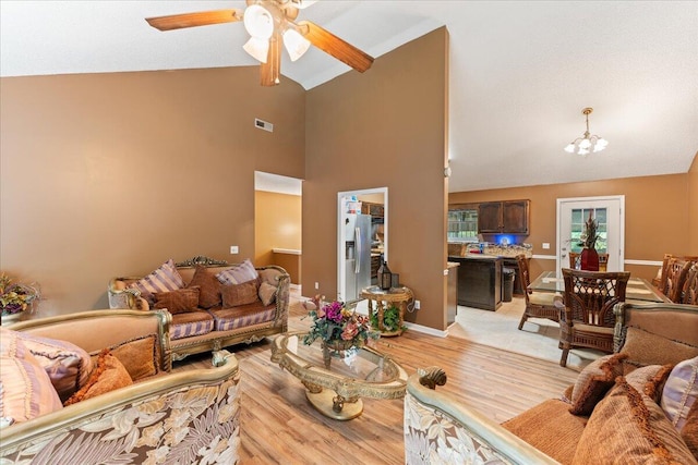 living room with ceiling fan with notable chandelier, light hardwood / wood-style flooring, and high vaulted ceiling