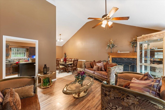 living room featuring ceiling fan with notable chandelier, light hardwood / wood-style flooring, a premium fireplace, and high vaulted ceiling