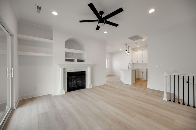 unfurnished living room with light wood-type flooring, crown molding, built in features, and ceiling fan