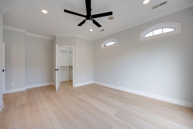 unfurnished bedroom with a spacious closet, a closet, ornamental molding, ceiling fan, and light wood-type flooring