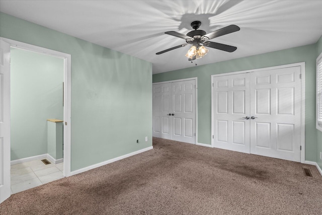 unfurnished bedroom featuring ceiling fan, light colored carpet, and two closets