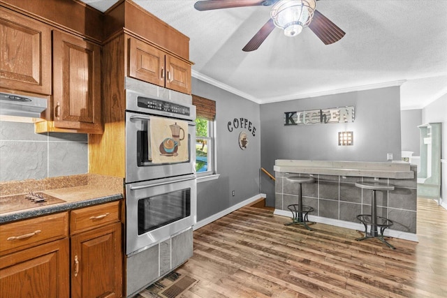 kitchen with hardwood / wood-style floors, crown molding, stainless steel double oven, a textured ceiling, and ceiling fan