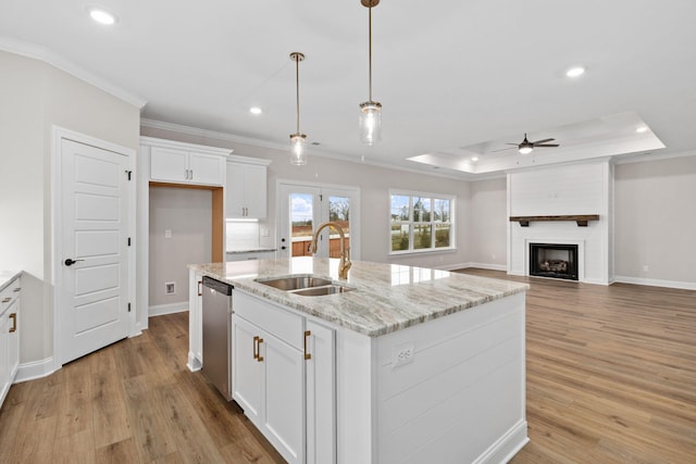 kitchen featuring stainless steel dishwasher, sink, white cabinets, a raised ceiling, and a center island with sink