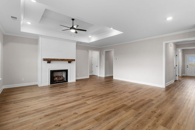 unfurnished living room with crown molding, a large fireplace, a raised ceiling, light hardwood / wood-style flooring, and ceiling fan