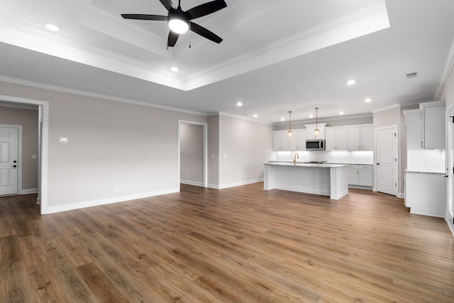 unfurnished living room with wood-type flooring, a tray ceiling, and ornamental molding