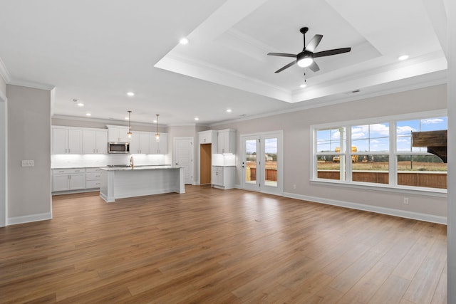 unfurnished living room with ornamental molding, a raised ceiling, and light wood-type flooring