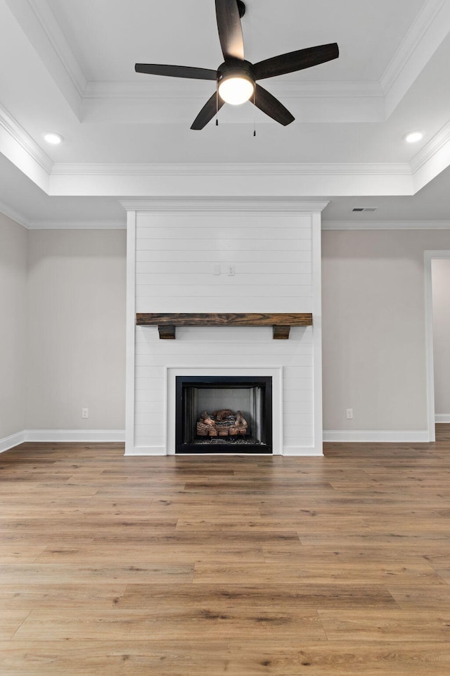 unfurnished living room with light wood-type flooring, a tray ceiling, crown molding, and a fireplace