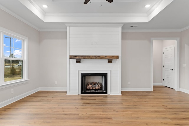 unfurnished living room featuring a large fireplace, crown molding, light hardwood / wood-style floors, and a raised ceiling