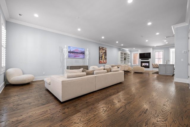 living room featuring a fireplace, dark hardwood / wood-style floors, built in features, and crown molding