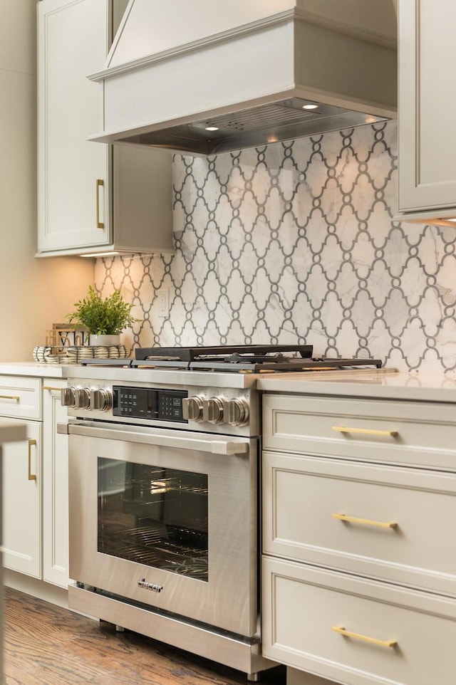 kitchen featuring backsplash, premium range hood, high end stainless steel range oven, light hardwood / wood-style flooring, and white cabinetry