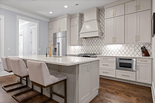 kitchen with sink, a kitchen bar, a kitchen island with sink, custom exhaust hood, and appliances with stainless steel finishes