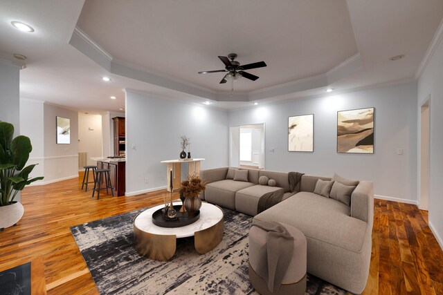 living room featuring wood-type flooring, a raised ceiling, crown molding, and ceiling fan