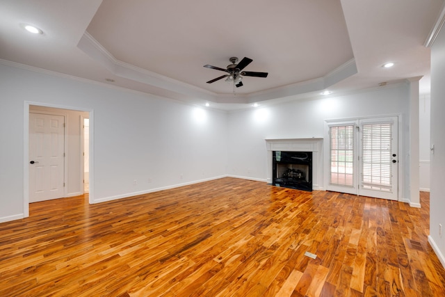 unfurnished living room featuring crown molding, a high end fireplace, light hardwood / wood-style flooring, a raised ceiling, and ceiling fan