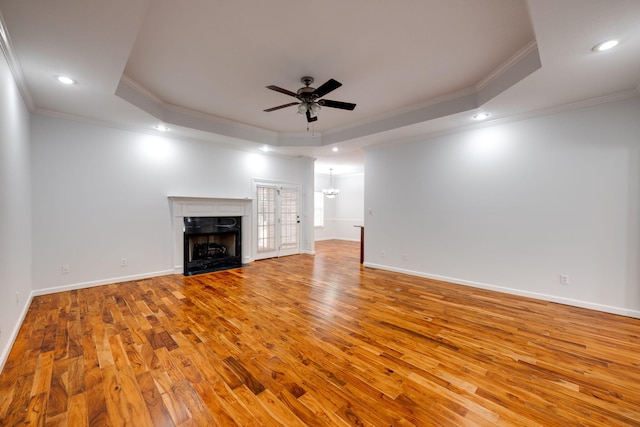 unfurnished living room with a tray ceiling, light hardwood / wood-style floors, crown molding, and ceiling fan