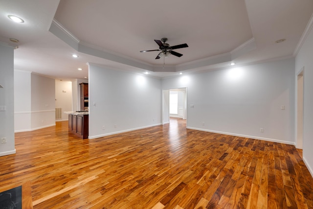 empty room featuring a tray ceiling, ornamental molding, wood-type flooring, and ceiling fan