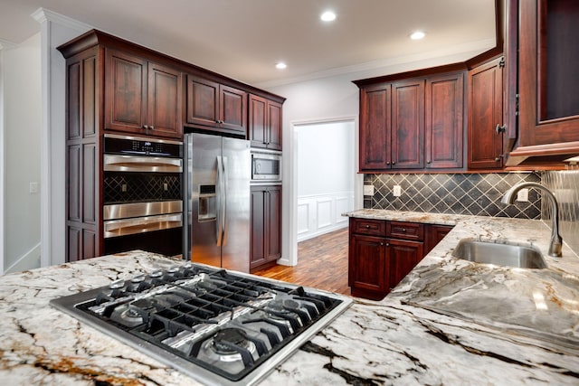 kitchen featuring crown molding, stainless steel appliances, sink, decorative backsplash, and light stone counters