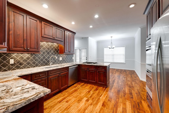 kitchen with hanging light fixtures, light hardwood / wood-style flooring, appliances with stainless steel finishes, light stone counters, and kitchen peninsula