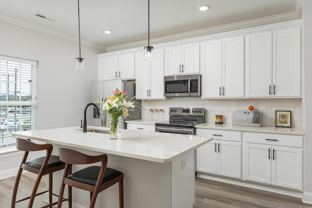 kitchen with a center island with sink, hanging light fixtures, stainless steel appliances, white cabinetry, and hardwood / wood-style flooring