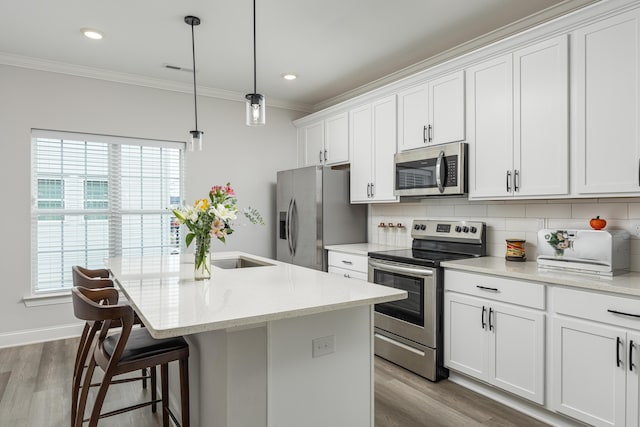 kitchen featuring wood-type flooring, a kitchen island with sink, stainless steel appliances, decorative backsplash, and white cabinetry