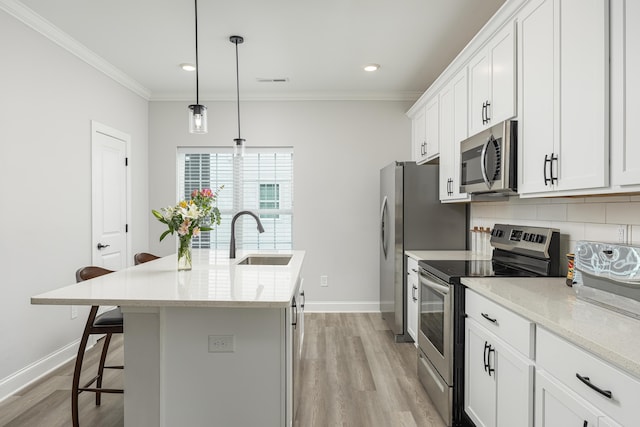 kitchen with light wood-type flooring, decorative light fixtures, sink, appliances with stainless steel finishes, and a center island with sink