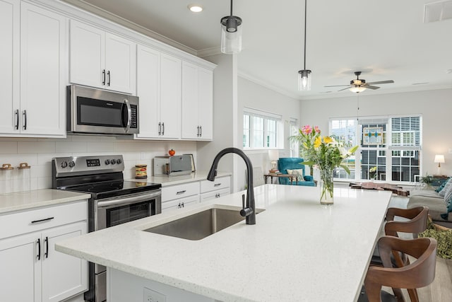 kitchen with stainless steel appliances, sink, ceiling fan, a breakfast bar, and a center island with sink